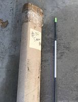 Cardboard tube containing snow markers plus one sample marker showing green shaft, white reflective band, green tip
