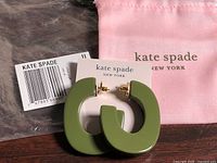 Front view of Kate Spade green resin hoop earrings on card alongside pink pouch and plastic bag