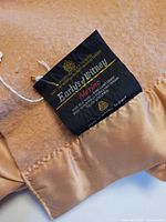 Close-up of Early's of Witney Merino label on peach wool blanket with satin trim