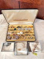 Open jewelry box showing assorted earrings, rings, brooches, bracelets and necklaces plus three small boxes