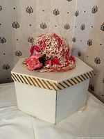 Straw hat with pink ribbons and flower on white hexagonal box