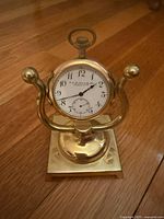 Front view of brass McLeod clock mounted on brass stand, showing dial, case and stand base