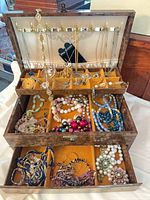 Open Mele jewelry box showing burl exterior, velvet interior, assorted necklaces, bracelets, brooches and earrings