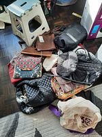Pile of various bags on floor showing quilted duffle, backpack, tote, clutches