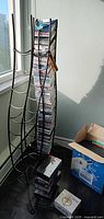 Metal CD tower filled with CDs beside metal wine rack and box with VHS tapes
