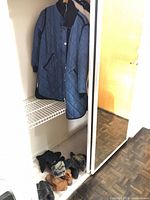 Closet view showing blue quilted coat, boots and gloves on floor