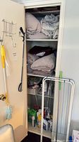 Closet view showing towels, sheet sets, cleaning products, drying rack, iron and steamer
