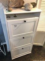 Front view of white three-tier shoe cabinet showing three compartments and top shelf