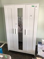 Front view of white three-door storage cabinet with mirror and handles