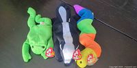 Group view of three Ty Beanie Babies plush toys: green frog, black/white skunk, rainbow inchworm, tags visible