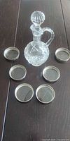 Crystal decanter with stopper surrounded by six coasters on dark table