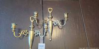 Pair of matching polished brass two-arm candle wall sconces on dark background