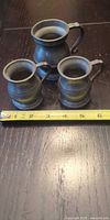 Three pewter mugs beside ruler showing relative sizes