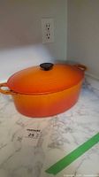 Full view of orange oval Le Creuset baker with lid on countertop