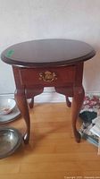 Full view of side table showing oval top, drawer, legs