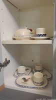 cabinet showing covered butter dish on plate and four oval egg servers below