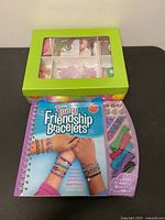 Front view of Klutz bracelet kit book beside green craft supply box