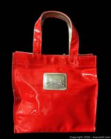 Front view of red PVC Harrods tote showing silver logo plaque and handles