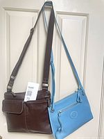 Front view of both brown and blue Roots bags hanging by straps