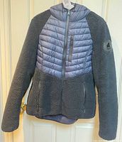 Front view of Pajar jacket showing polar fleece sleeves, blue chevron-quilted chest section, zip pockets and hood