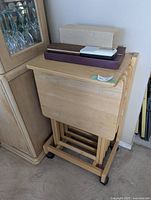 Stacked items atop TV tray stand showing trays, Scrabble box, storm bottle box, radio and pen case