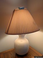 Full view of one lamp showing ceramic base and pleated shade lit