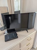 Front view of Sharp 32-inch TV on dresser with remote and excluded Motorola box visible
