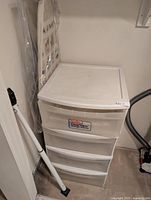 Full view of Sterilite drawer unit with ironing board behind and security bar leaning