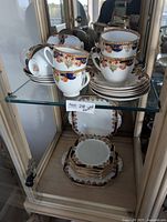 Overall view of set on two shelves showing teacups, saucers, round plates, square plates and handled serving plate