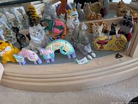 Mixed cat figurines on bottom shelf including porcelain Garfield, grey cat, pastel wooden cats, black figurines
