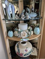 Three-shelf display showing large round floral vase, iridescent vases, pillar candle with floral ring