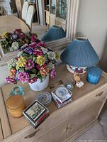 overall view of lamp, faux flowers, candles, Caithness clock, coasters and wood cat napkin holder on cabinet top