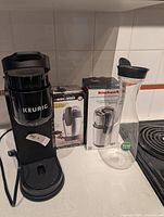 Front view of Keurig machine, boxed grinders, glass carafe