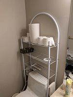 Full view of white metal over-the-toilet rack positioned over toilet
