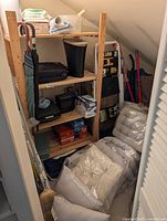 Overall view of storage closet contents including shelving unit, patio cushions, ladder, umbrellas, broom