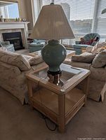 Side table with glass top and teal lamp placed on it, sofa background