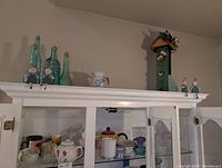 Top of hutch showing aqua glass bottles, small pitcher, wooden birdhouse tower, ceramic figurines and inside shelf items