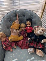 Group shot of all five items on chair: two teddy bears, three dolls