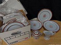 Box containing stacked Spode Red Newburyport dishes, creamer, sugar bowl