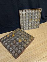 Two square iron chocolate mold trays with grid of cavities