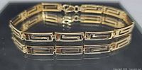 Greek key gold bracelet front view on reflective surface