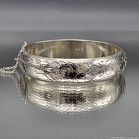Full view sterling silver engraved hinged bangle on reflective surface