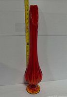 Full view of red Amberina swung glass vase beside tape measure showing ~21 in height