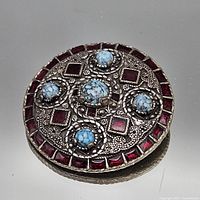 Front view of round brooch showing turquoise cabochons and red stones