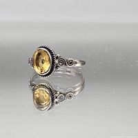 Profile view of sterling silver ring showing faceted oval yellow gemstone and scroll shoulder detail