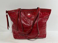 Front view of red patent leather Coach tote showing embossed monogram and logo medallion