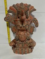 Full front view of terracotta Zapotec style sculpture with measuring tape showing height