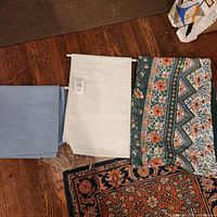 three folded tablecloths: solid blue rectangle, solid white rectangle with label, patterned floral oval