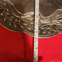 Close-up of tray edge showing butterfly and leaf relief with measuring tape indicating width