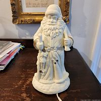 Front view of white ceramic Santa figurine showing gold accents and cord